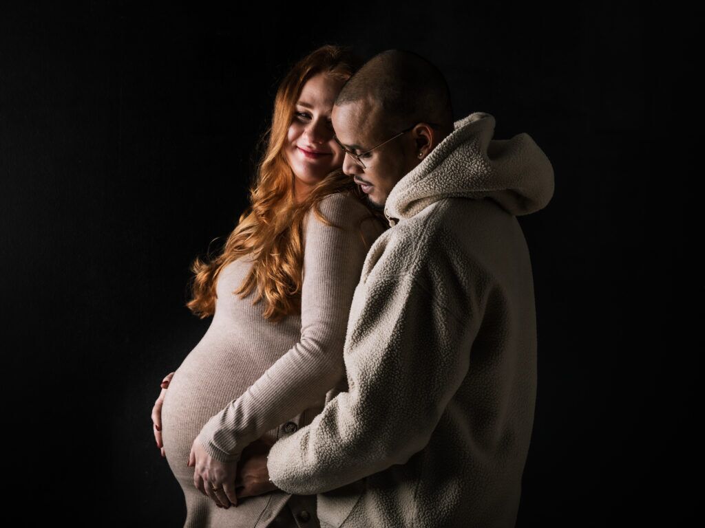 Zwangere vrouw en partner houden elkaar liefdevol vast donkere achtergrond